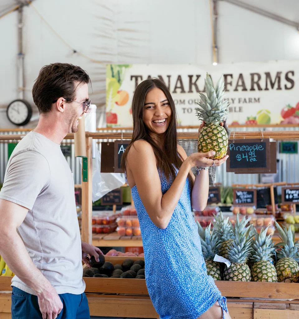 girl holding a pineapple with boy smiling at her at tanaka farms