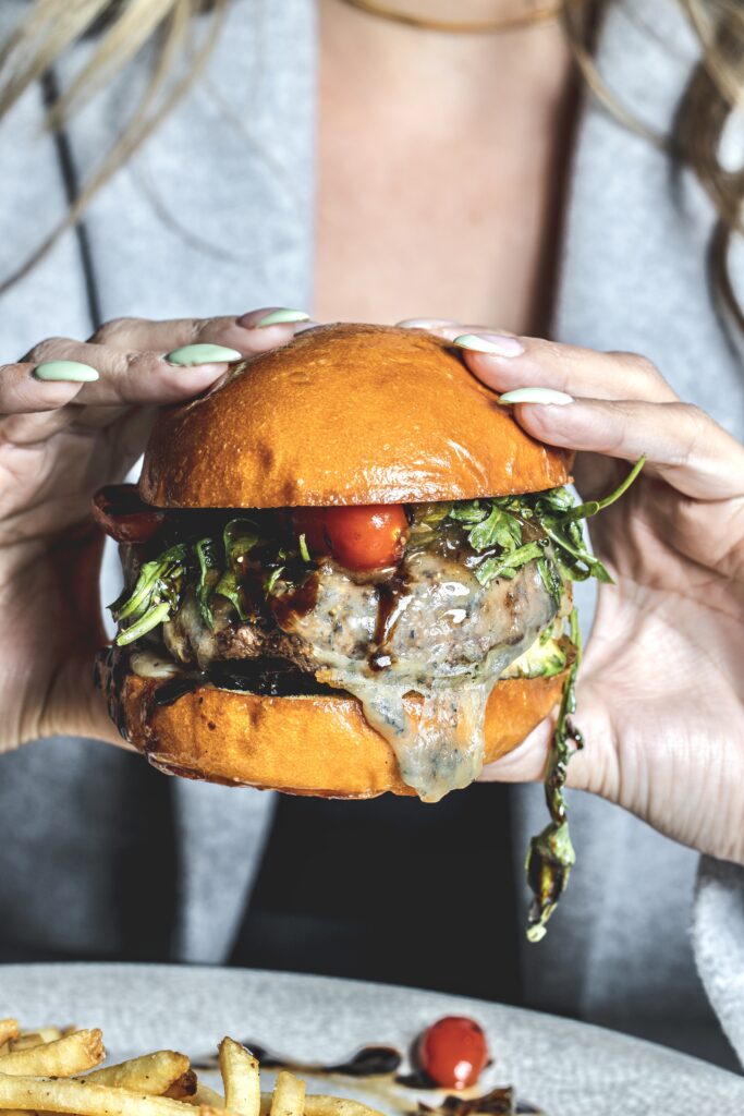hand with sea green nail polish holding a juicy burger