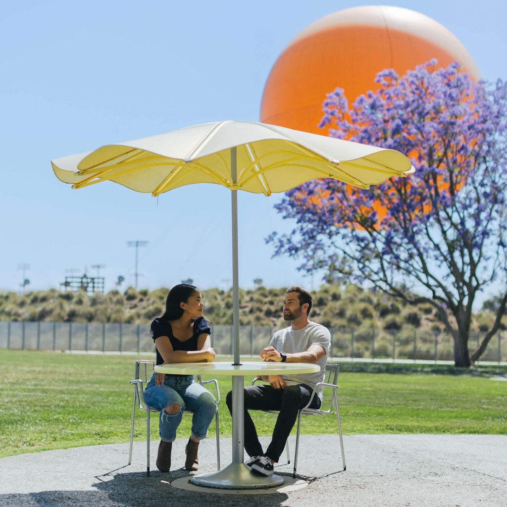 3 天行程 2 couple sitting on silver chairs with yellow table under an umbrella with view of great park balloon and purple trees