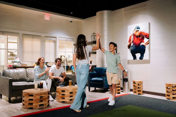 girl and boy doing a high five inside irvine marriott topgolf suite with mom and dad sitting on couch smiling and clapping with drinks in table