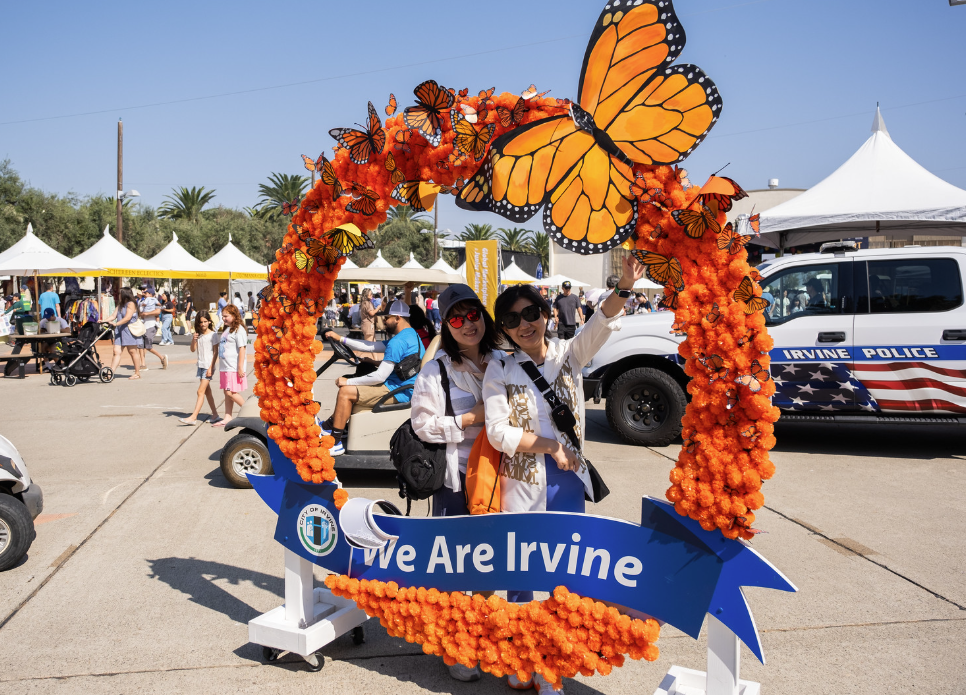 round orange photo op with monarch butterfly and slogan we are irvine with two ladies posing