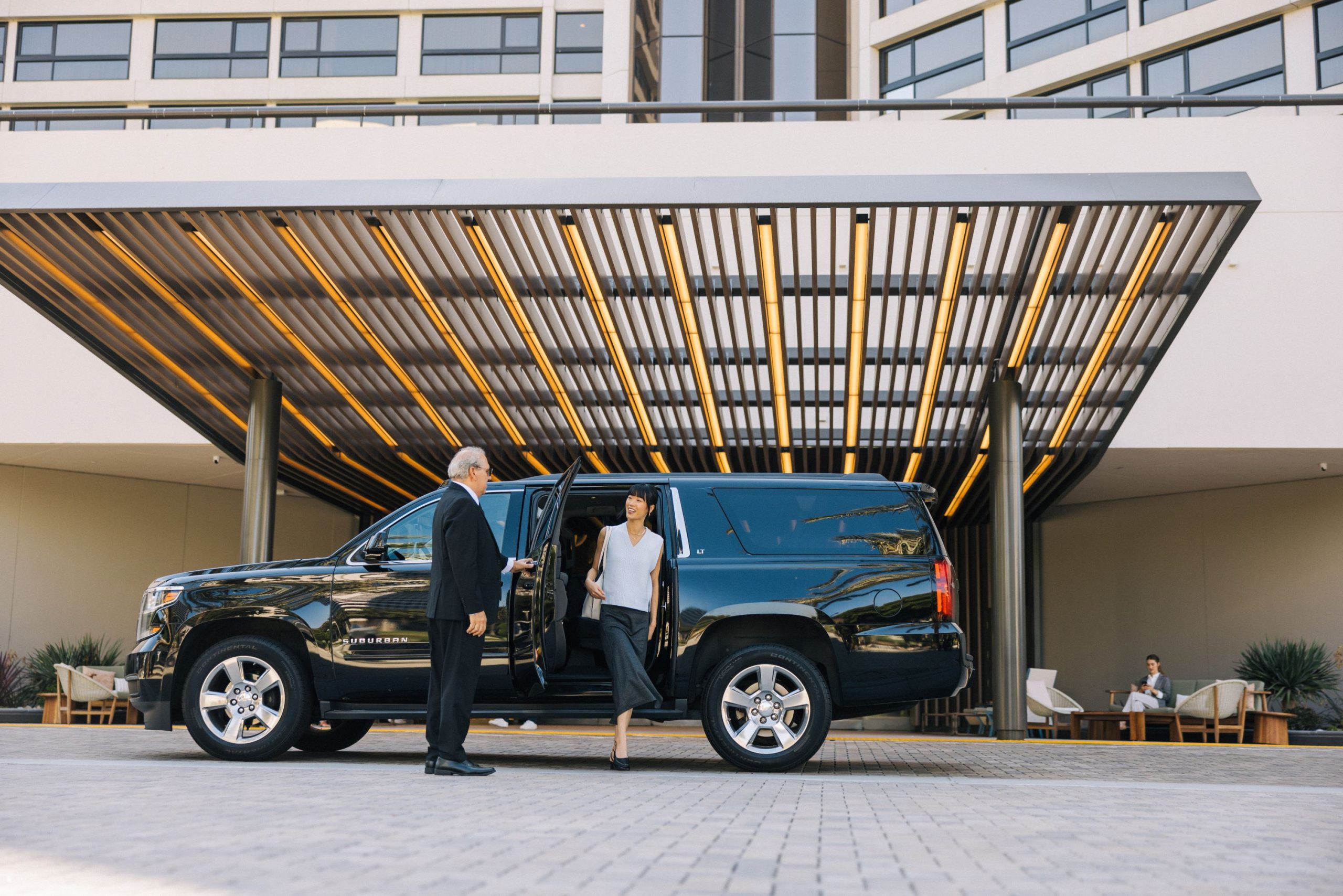 woman stepping out of black vehicle with chauffeur at hotel entrance