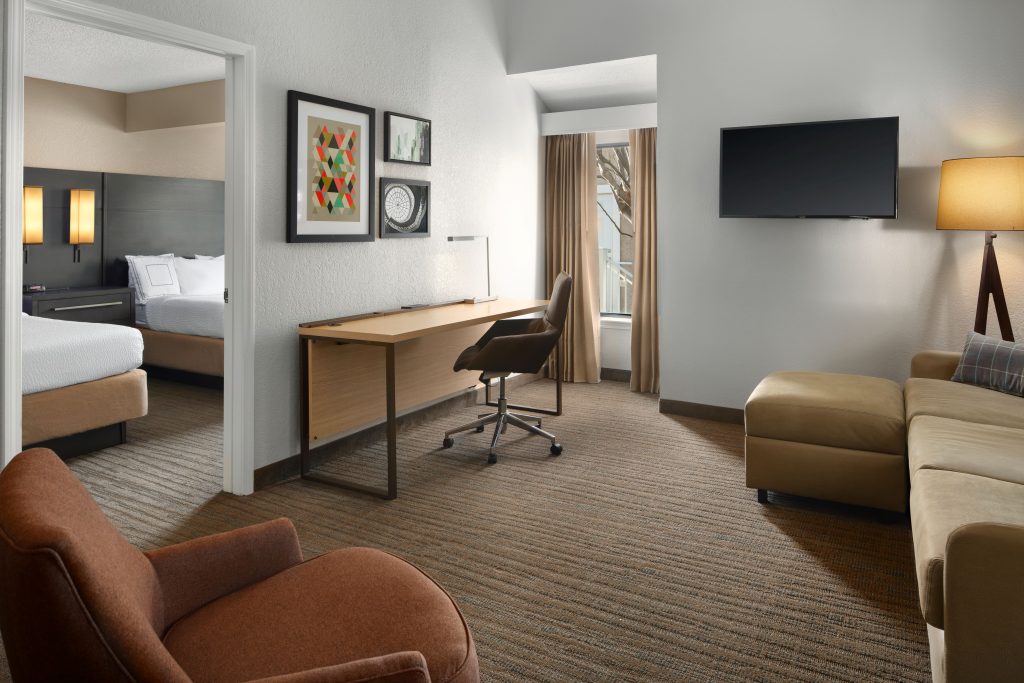 room suite at residence inn irvine spectrum with 2 beds desk chair sofa lamp and picture frames on the wall