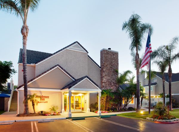 exterior of Residence Inn Irvine Spectrum Hotel at night withh lights lit up at the entrance with the American flag and palm trees