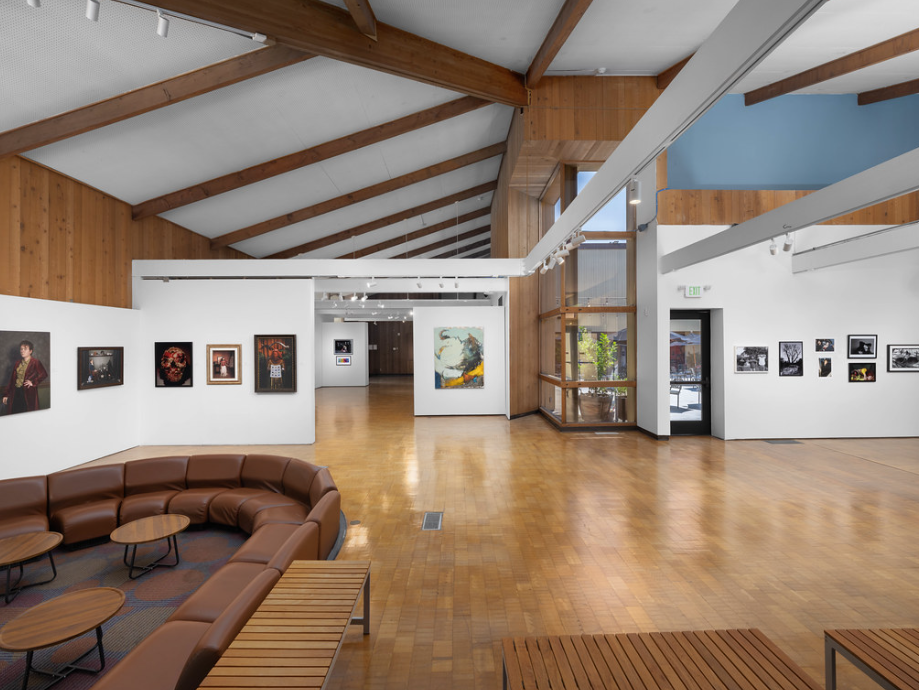 art gallery with brown couch wooden floors white walls with frames displayed at irvine fine arts center