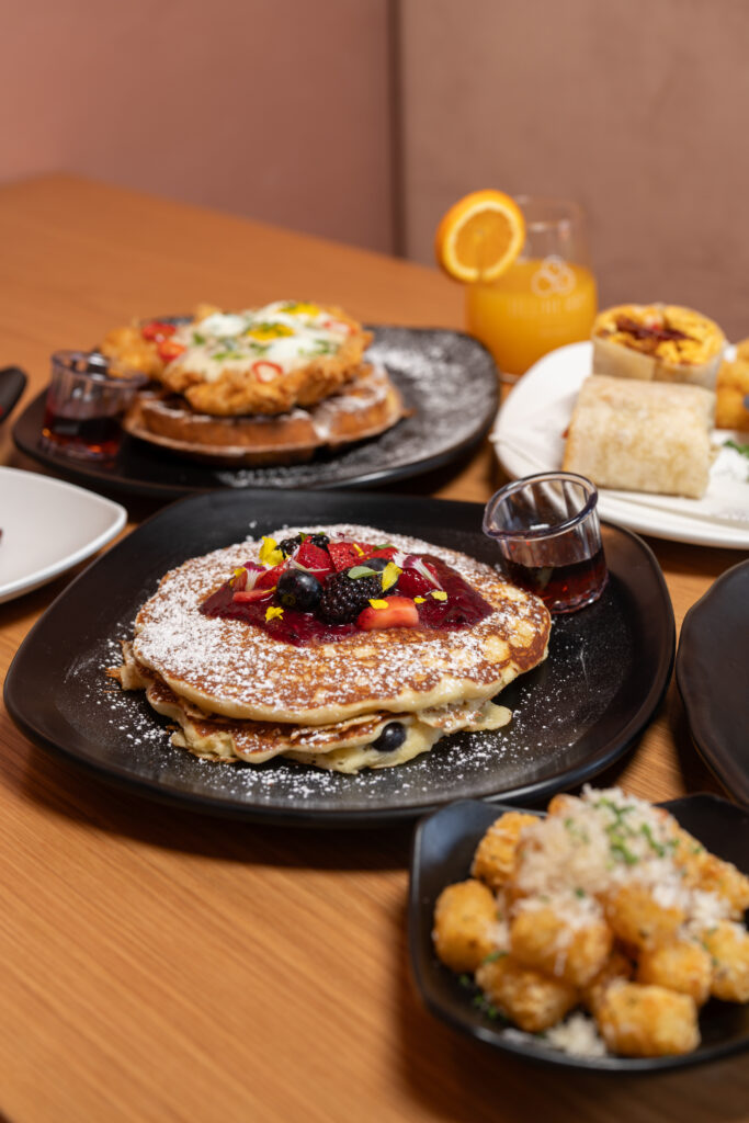 table with pancakes, chicken waffles, tater tots, burrito and orange juice