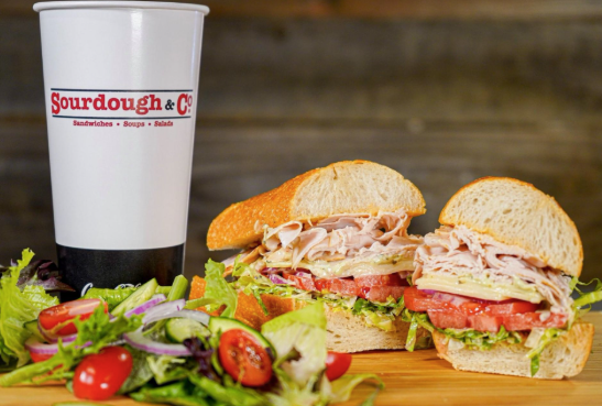 soda cup with sourdough and co printed on it and sandwich cut in halves and vegetables
