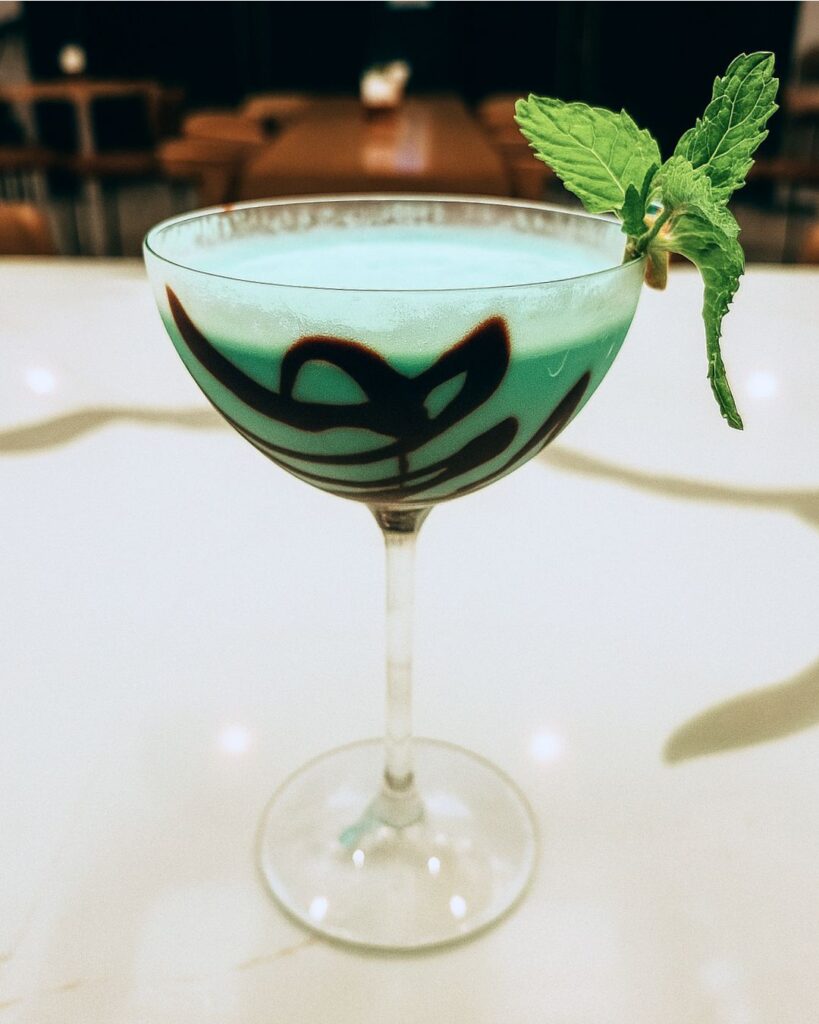 a green colored cocktail drink with a left that looks like a dragon