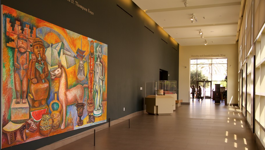 museum hallway with paingting of a man, woman, horse against a black wall with rays of sun on the other side