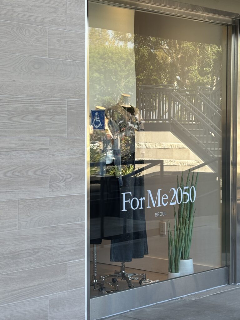 retail store glass window display with store name For Me 2050 Seoul on the glass with a headless mannequin and two plants inside the store