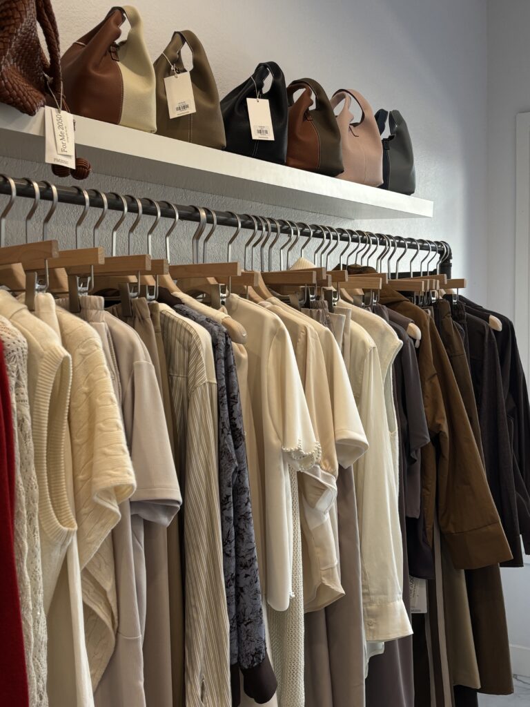a rack of clothes from cotton shirts to knits in beige white and brown colors with bags on top