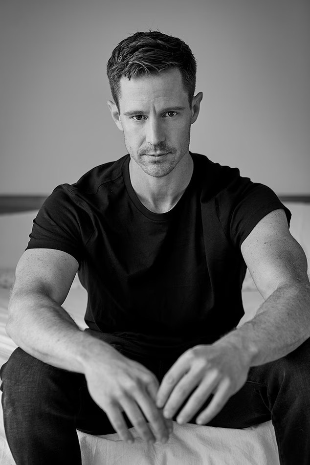 black and white photo of man sitting in fitted shirt and muscular arms
