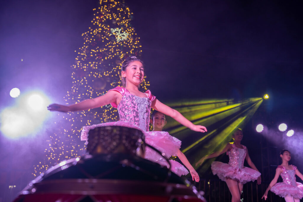 A Jolly Irvine Holiday 1 a young ballerina in tutus performing onstage with a huge christmas tree at the back