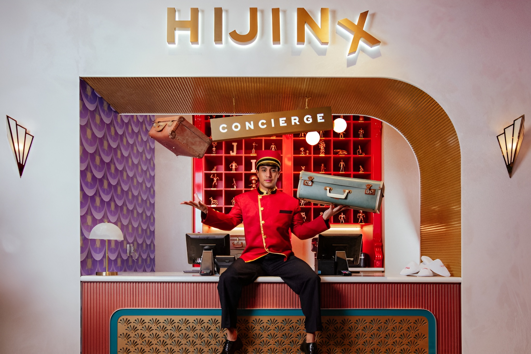 a bellboy in red sitting on top of the hotel front desk with hijinx at the top