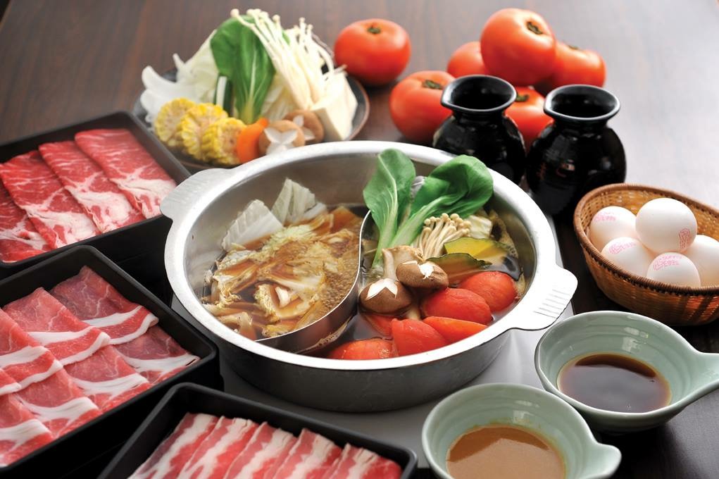 table of shabu shabu with plate sof raw meat, eggs, dips, sauces and a silver hot pot with raw meat, soup and vegetables