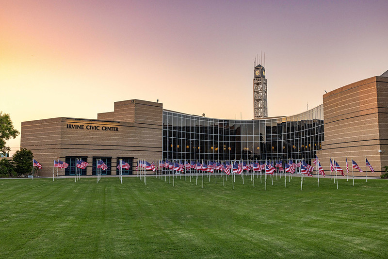a beige building with a clock tower and American flags in front of a green lawn