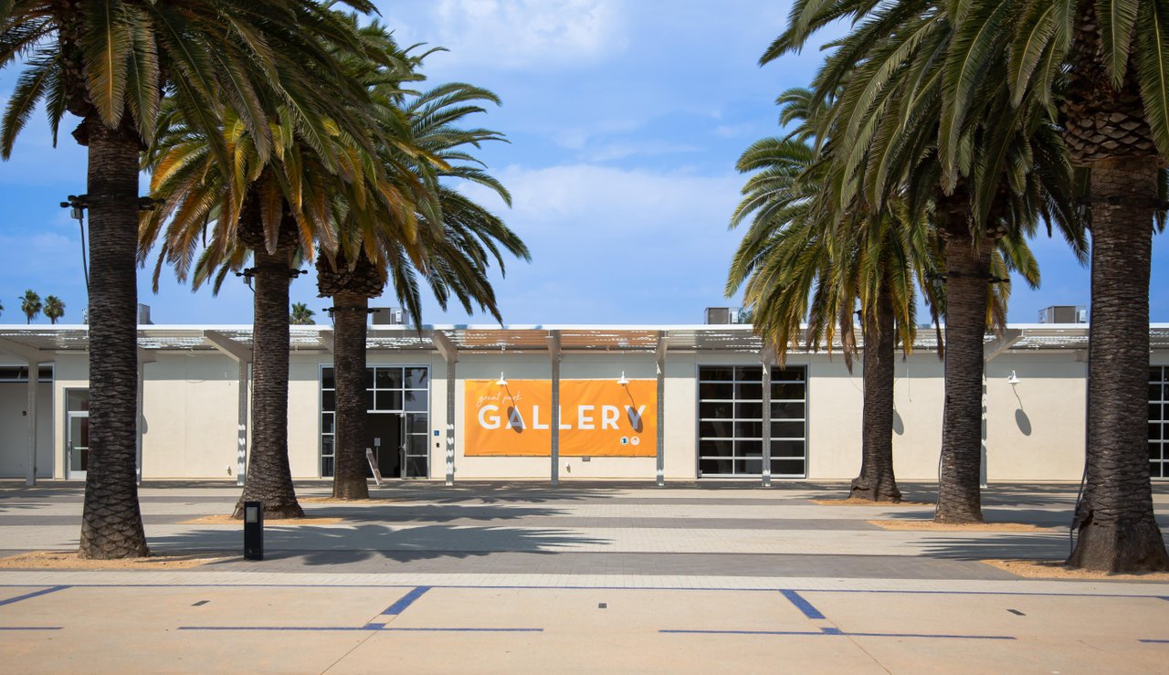 beige building with orange banner saying great park gallery with palm trees lined in front of the building