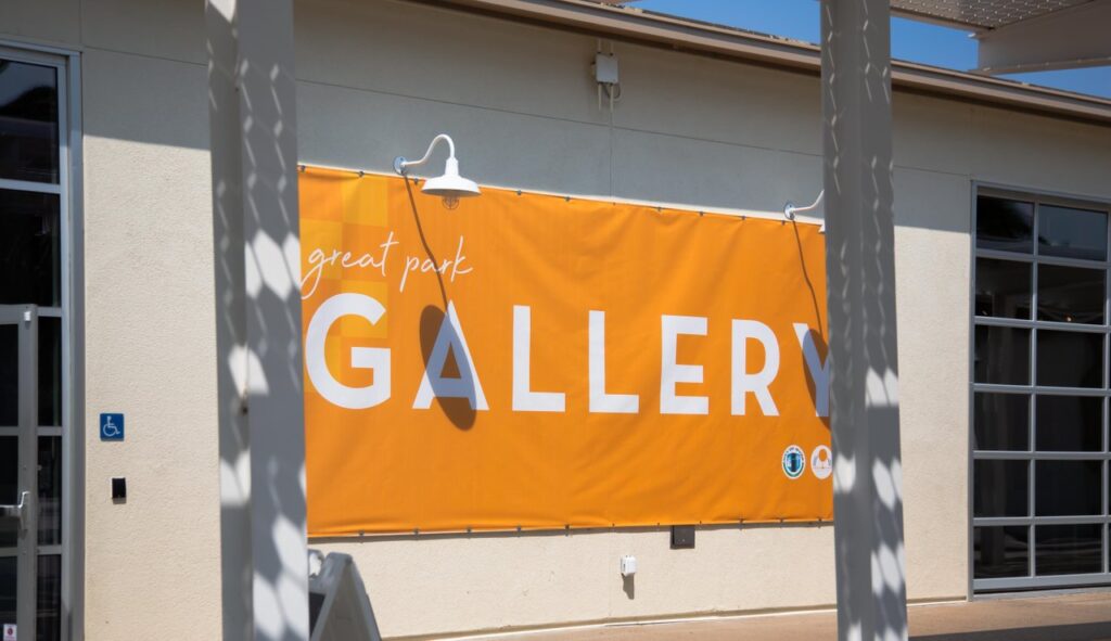 outside of a beige building with a banner that says great park gallery with orange background