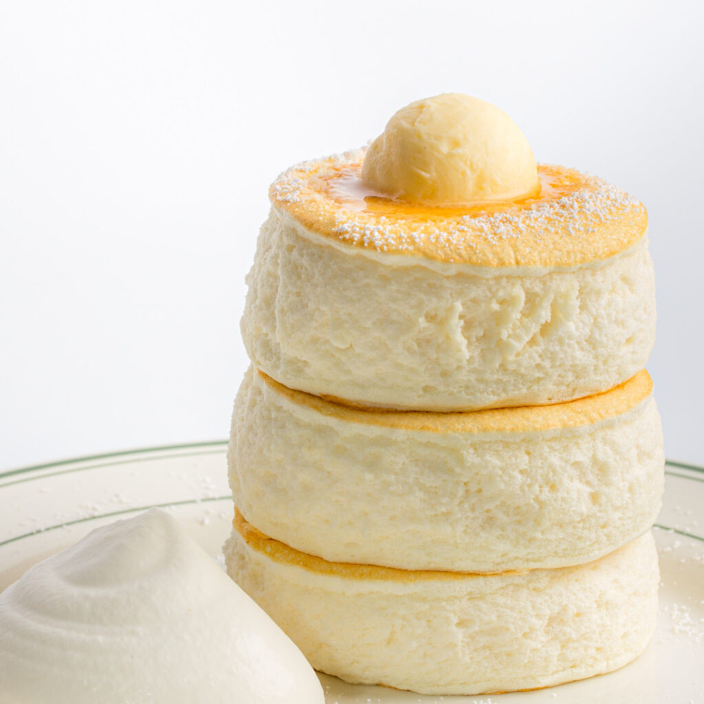 a plate of 3 stack fluffy pancakes with butter on top and cream on the side