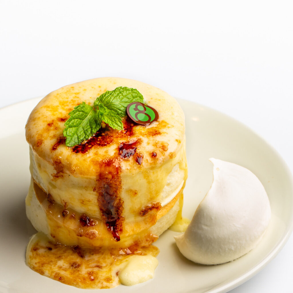 a plate of 3 stack fluffy pancakes with syrup and green garnish on top and cream on the side