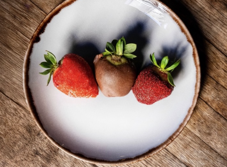 three red strawberries on a white plate and the center strawberry is dipped in chocolate