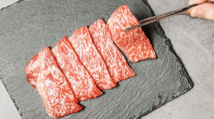 5 pieces of raw meat on top of a black serving dish