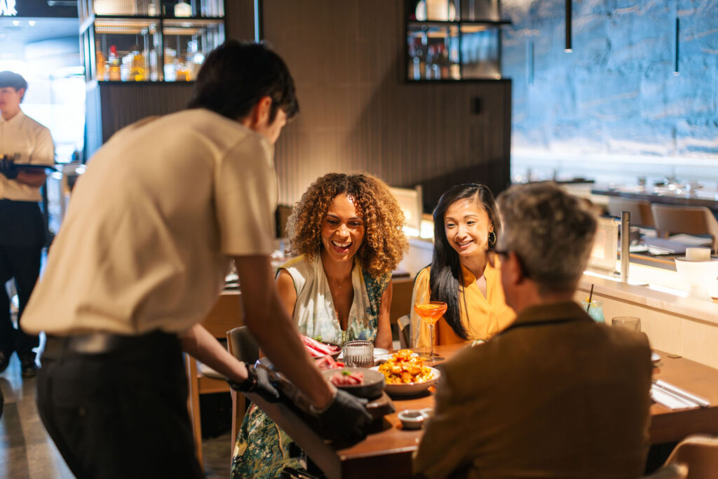 two females and 1 male at a restaurant with a waiter serving them food