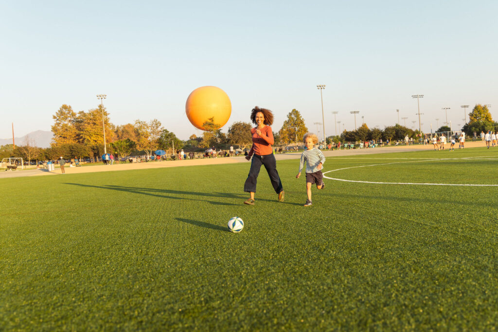mother and son playing soccer on a field with the orange helium balloon in the background