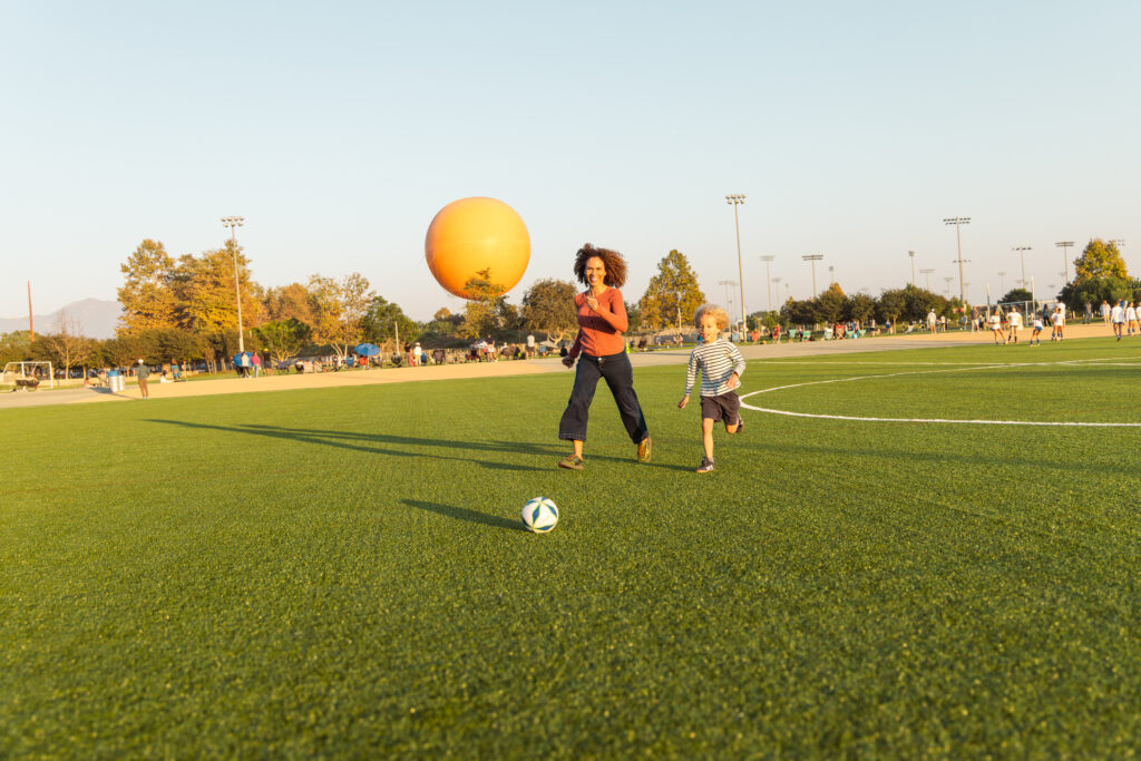 mother and son on a field playing soccer with an orange helium balloon in the background