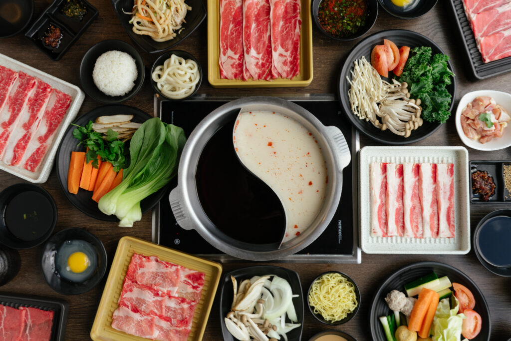 a table filled with plates of raw meat with a shabu shabu in the middle