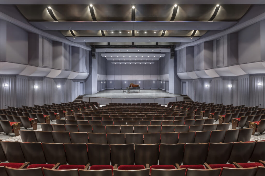 interior of theater with red seats and a grand piano onstage