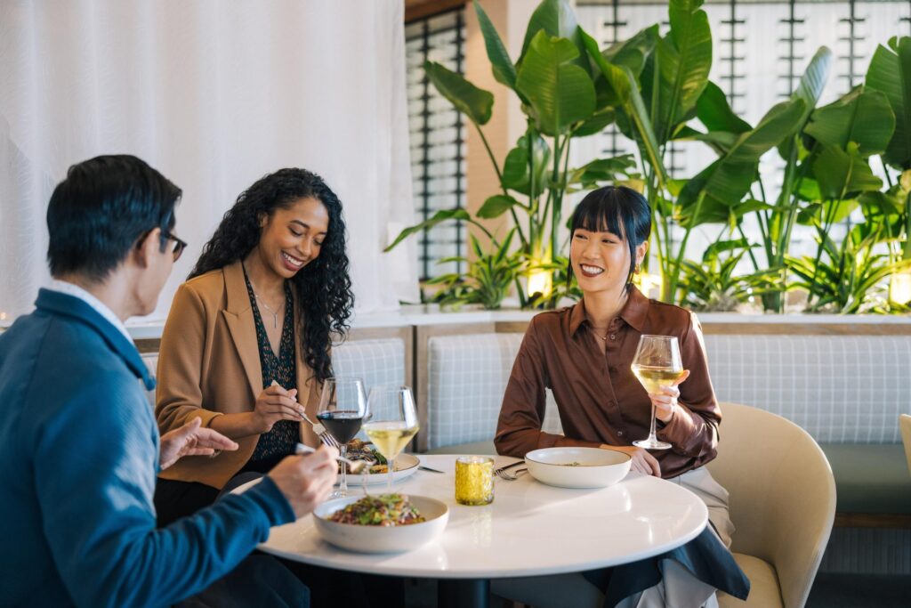 two women and one male dining at a restaurant each with a glass of wine and food on their table