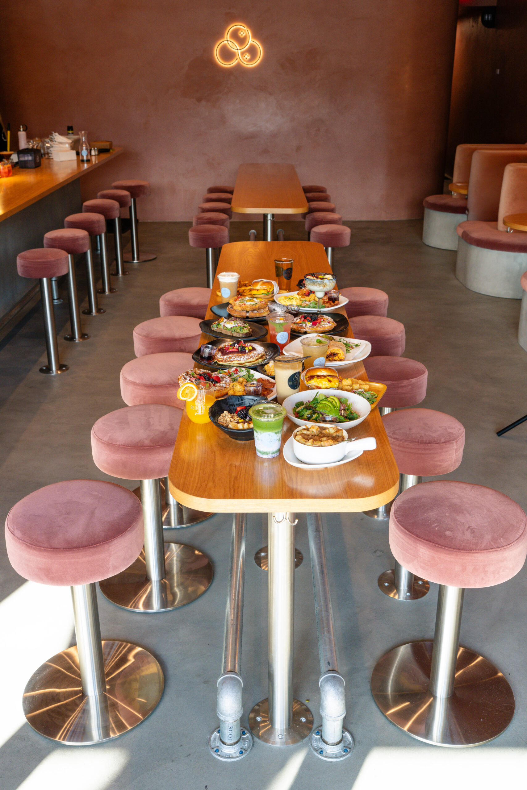 Interior of Bluberry Social restaurant with long rectangular bar height table and pink cushioned bar stools