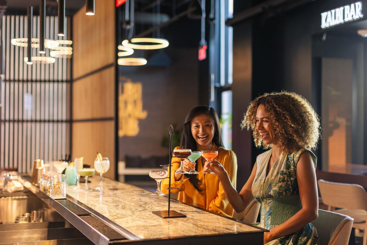 two ladies at a bar holding cocktails toasting