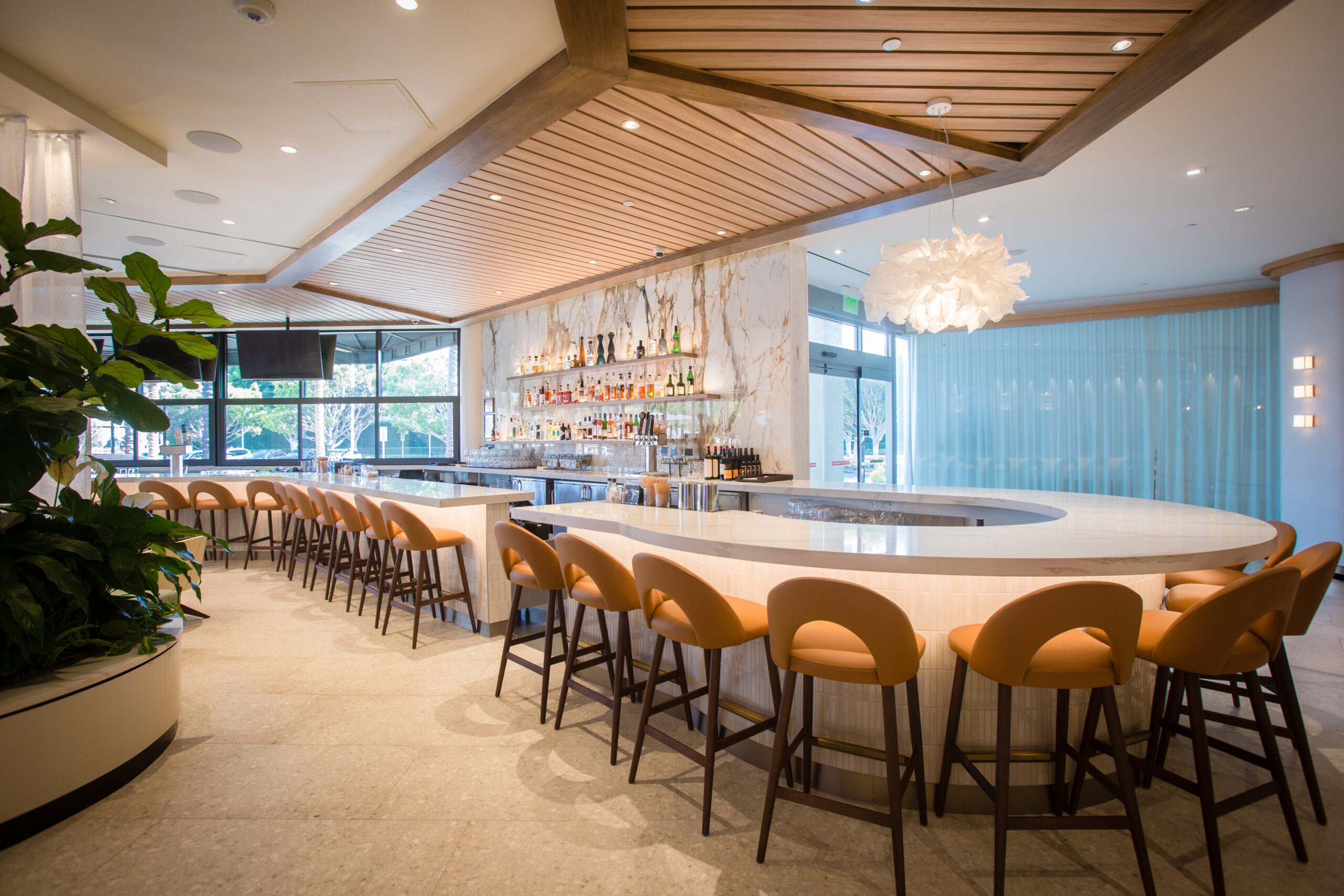 a beautiful bar with a curved corner, with a small white light hanging at the end of the bar and alcohol displayed at the middle center part of the bar
