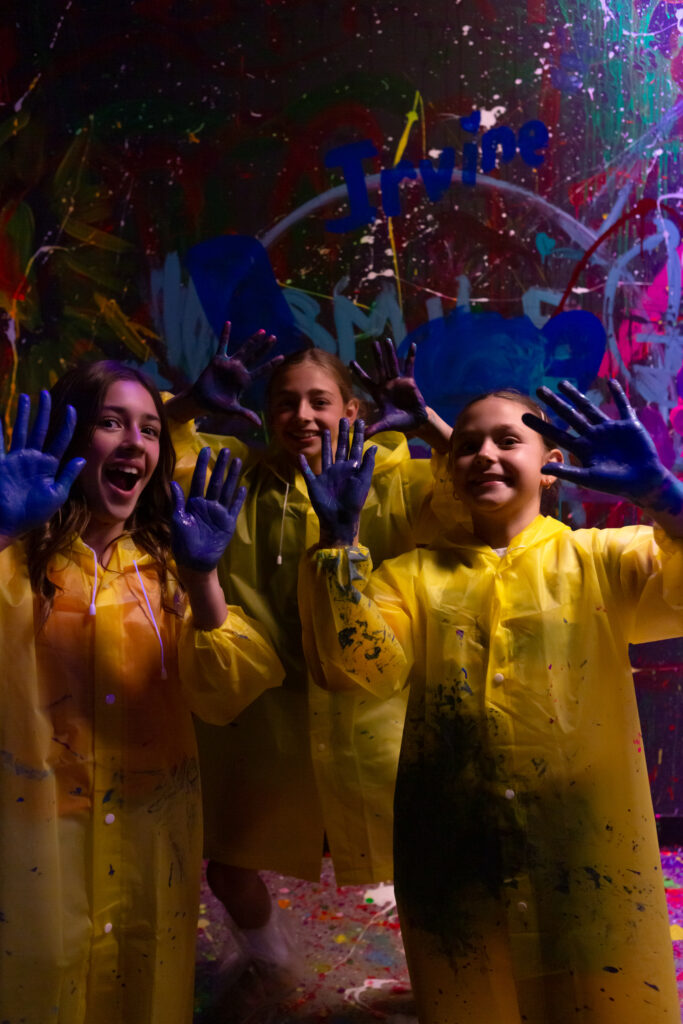 three young girls in yellow raincoat showing their hands filled with paint