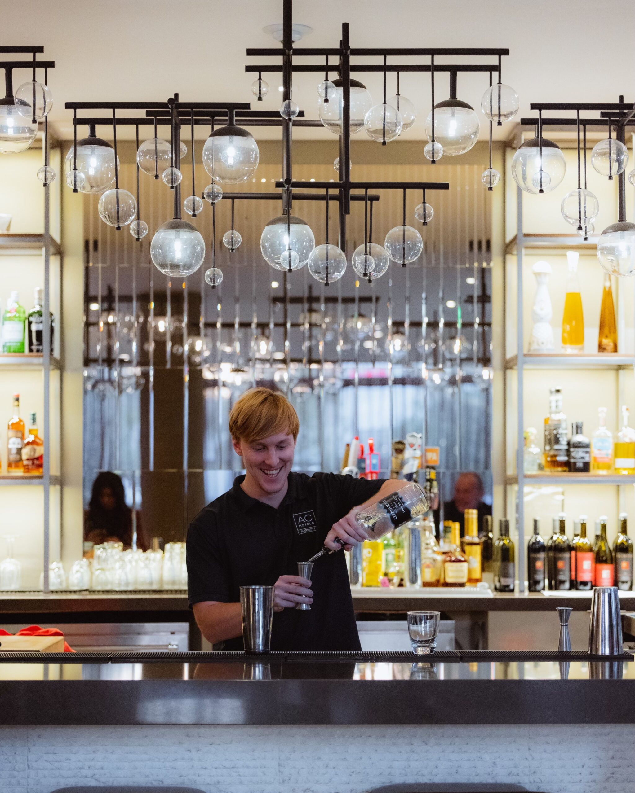 bartender in black AC Hotel polo shirt making a cocktail