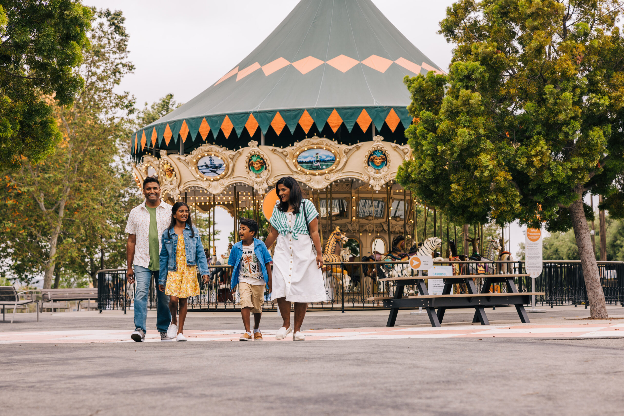 father, mother, daughter and son walking in a park with a carousel behind them