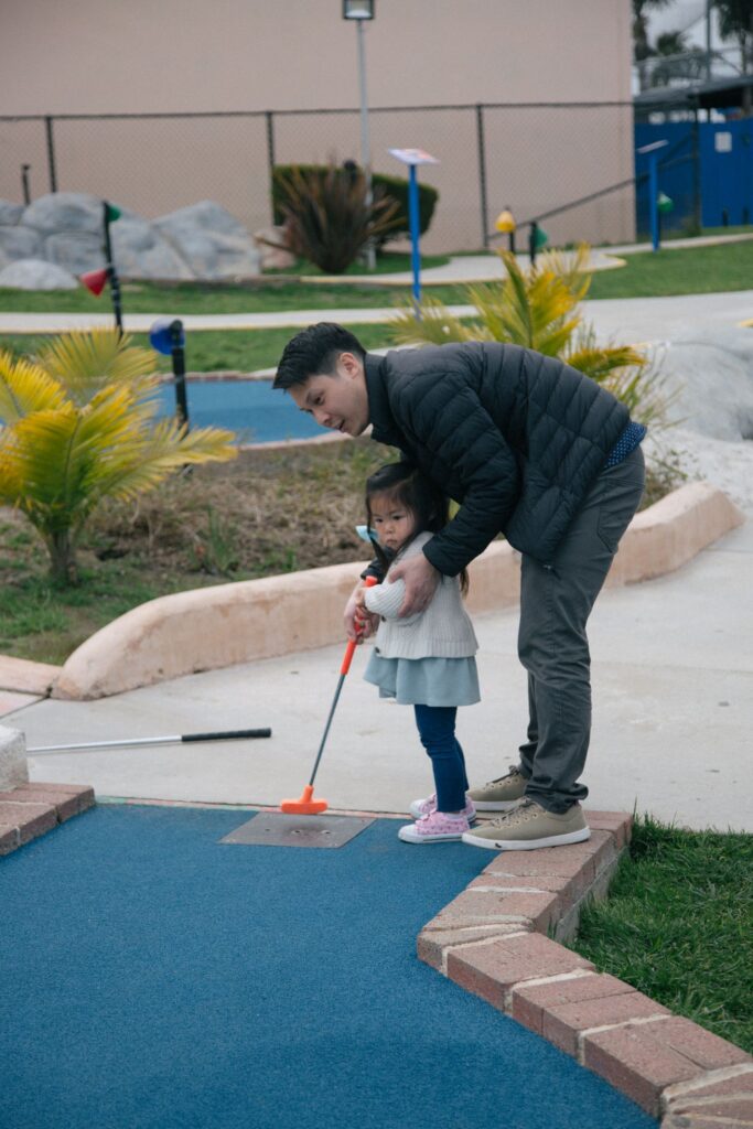 father teaching young daughter how to putt