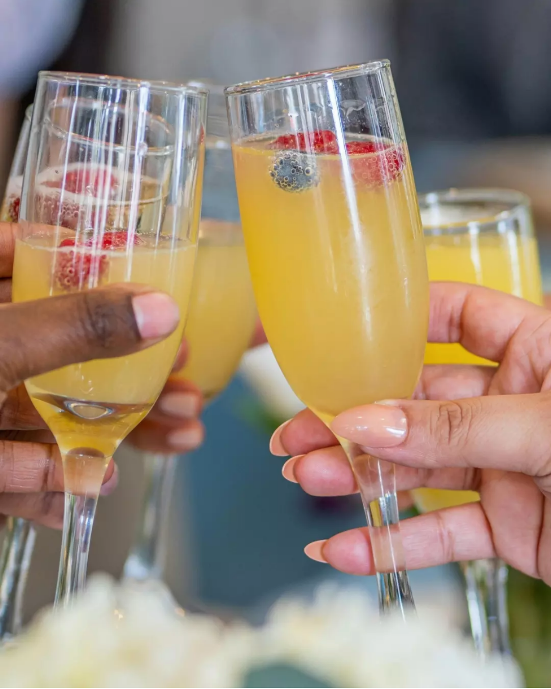 hands toasting flutes with mimosas