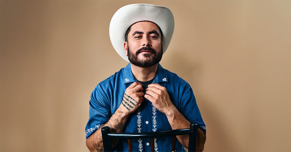 bearded man in blue polo shirt holding his collar wearing a white cowboy hat