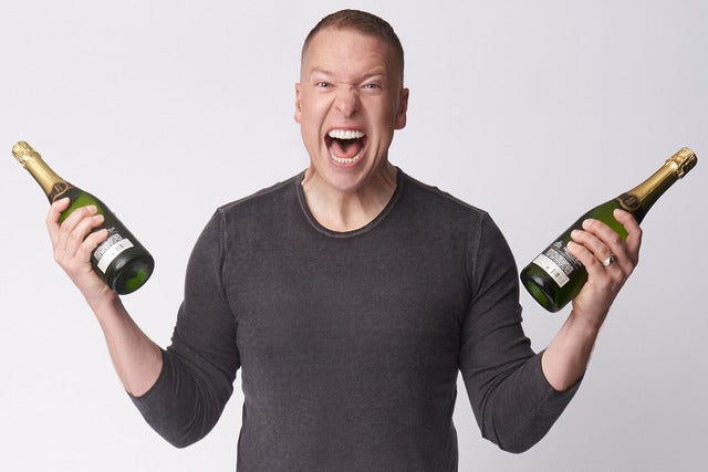 photo of man in plain black long sleeve holding a bottle of wine in each hand with mouth wide open