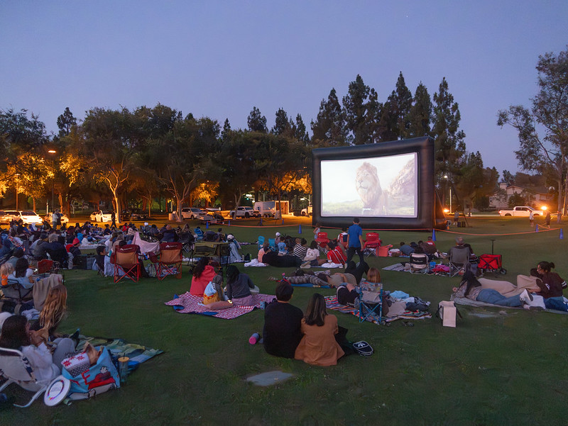 people sitting on blankets on the grass at dusk watching a huge screen in front