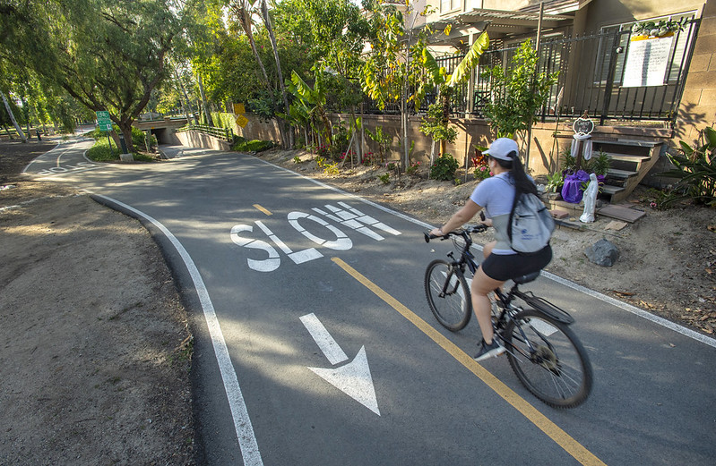 woman in black shorts riding a bike in a paved trail with slow and arrow sign painted on the pavement