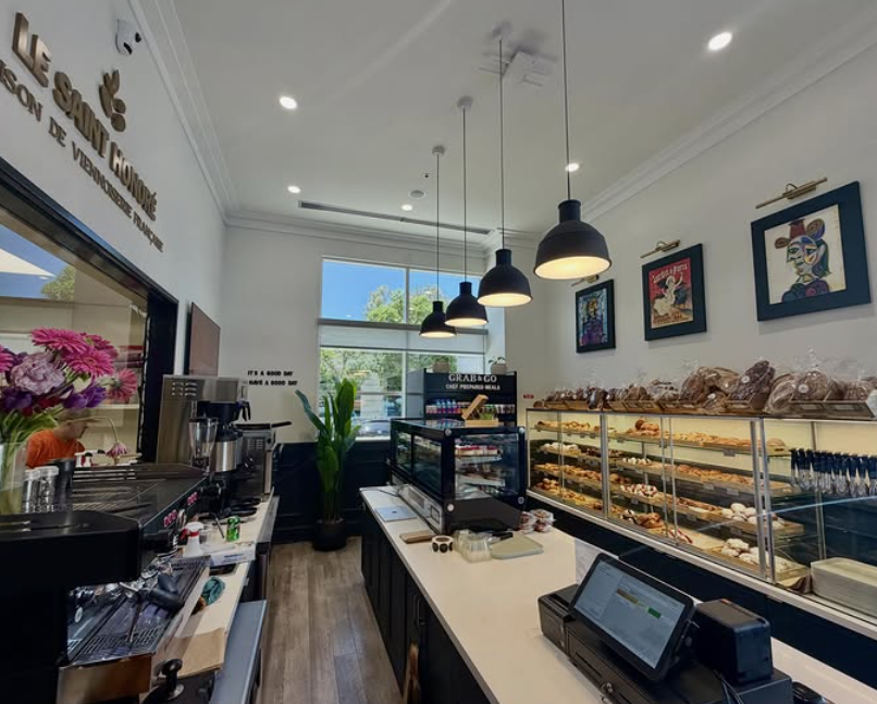 interior of bakery with Le Saint Honore on the wall, a cashier counter, a glass of pastries, and a vase of flowers