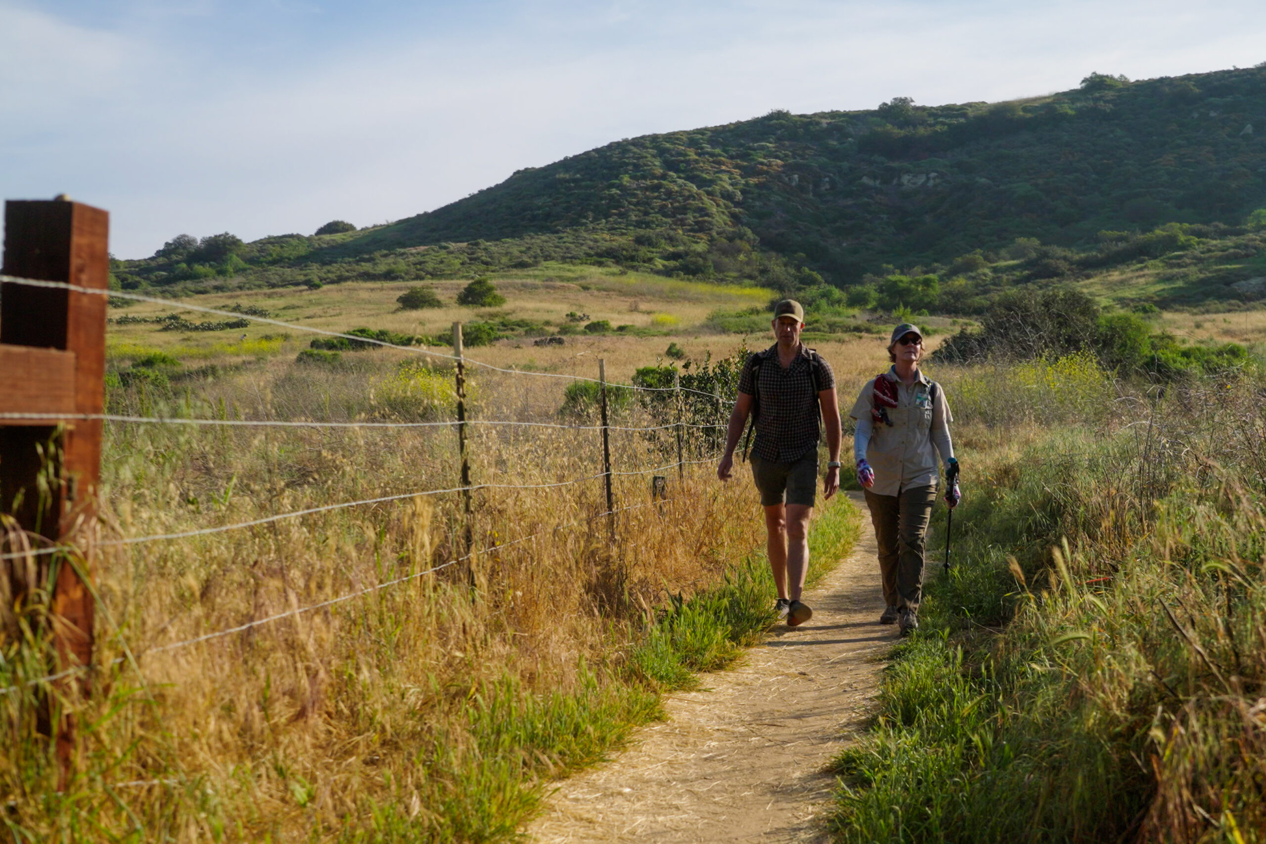 man and woman walking down a trail amidst hills