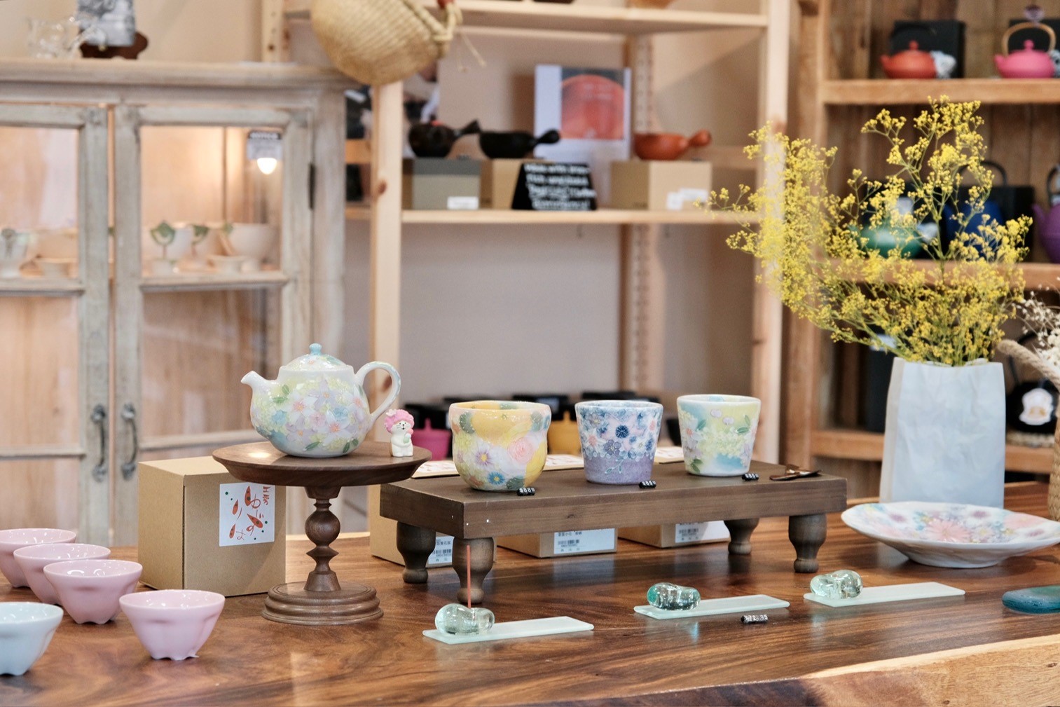 store with wooden table filled with colorful ceramics, teapot and flower vase as well as shelves with ceramics