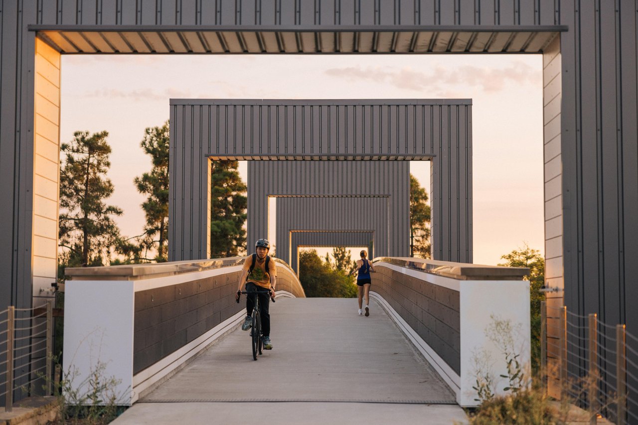 a boy biking and woman running on a bridge at Great Park