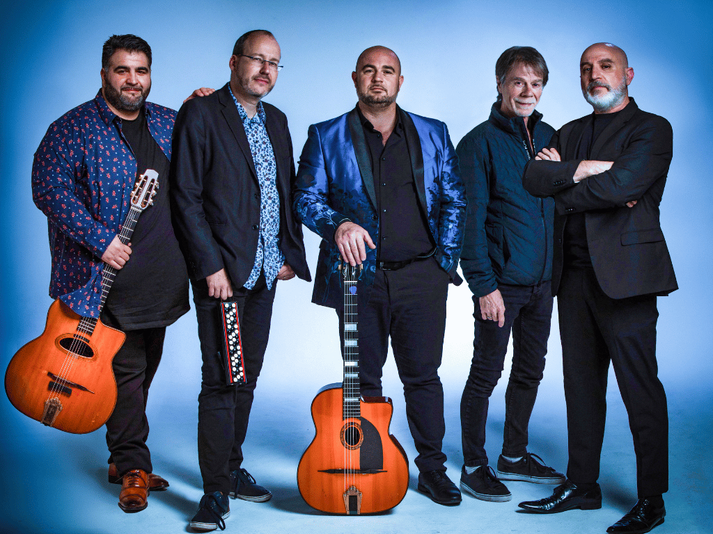 five male musicians in dark suits with 2 holding guitars