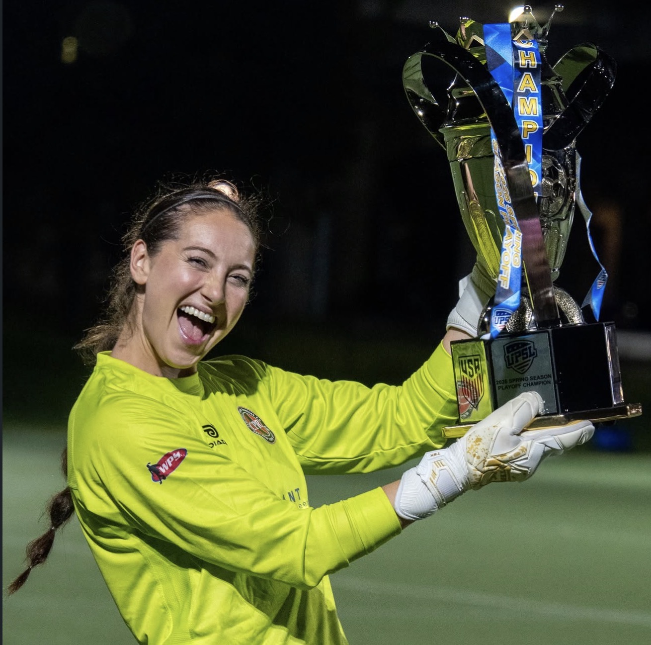 female athlete in neon yellow smiling, holding a trophy